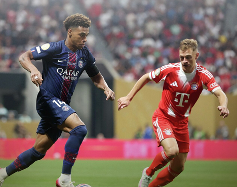 Два футболиста соперничают за мяч на поле. Игрок в форме синих тонов противостоит спортсмену в красно-белой форме. На заднем плане размыт фон с болельщиками на трибунах